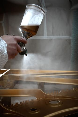 Hand mit Lackierpistole und Becher beim Lackieren einer Steinway & Sons Gussplatte